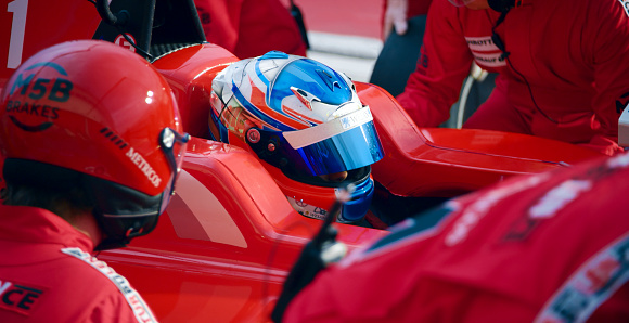 Pit crew in red uniform working on open-wheel single-seater racing car car at pit stop.