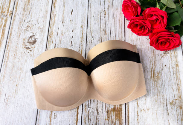 beige and black strapless nude bra on a wooden texture background next to rose flowers . Copy space for text input on health care and fitness. Balconette bra and lingerie for woman, top view. beige and black strapless nude bra on a wooden texture background next to rose flowers . Copy space for text input on health care and fitness. Balconette bra and lingerie for woman, top view. strapless stock pictures, royalty-free photos & images