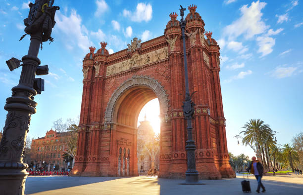Sunrise at Triumphal Arch in Barcelona, Catalonia, Spain. Sunrise at Triumphal Arch in Barcelona, Catalonia, Spain. Arc de Triomf at boulevard street. Alley with tropical palm trees. Early morning landscape with shadows and blue sky with clouds. Famous arc de triomf barcelona stock pictures, royalty-free photos & images