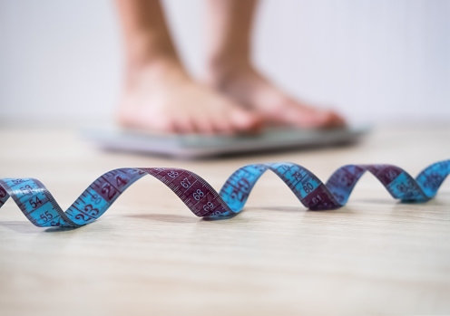 Spiral of a centimeter soft focus close up. Woman with bare feet measures her weight on blurred background. Female legs stand on weigh scales. Healthy lifestyle, food, slimming and sport concept.