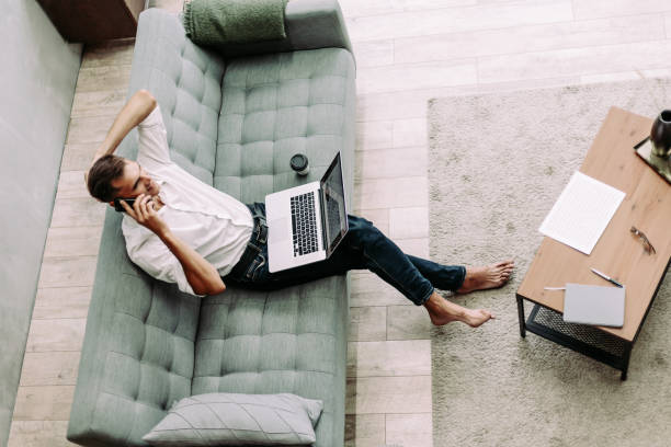 istock young man is talking on a smartphone, sitting on the sofa 1282477366