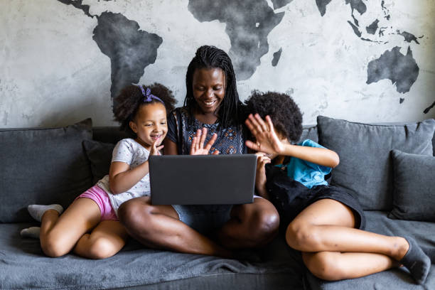 istock Young afro American mother with her daughters sitting on sofa doing video call 1282479817