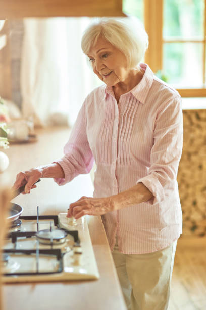 istock Happy elder lady standing in the kitchen and preparing food 1282480322