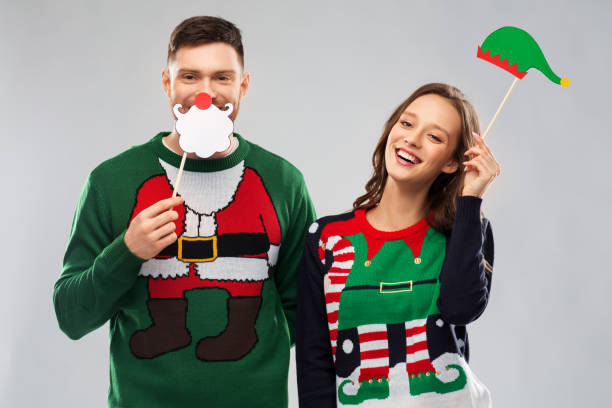 couple with christmas party props in ugly sweaters christmas, photo booth and holidays concept - happy couple in ugly sweaters posing with party props ugliness photos stock pictures, royalty-free photos & images