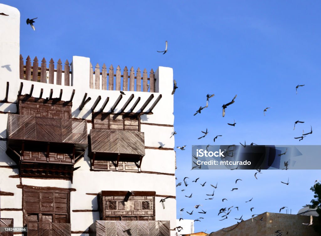 Al Balad district - pigeons and hedjazi architecture - arabian balconies, Suq Al Alawi - Historic Jeddah, Saudi Arabia - UNESCO world heritage site Jeddah, Mecca Region, Saudi Arabia: pigeons in Suq Al Alawi - hedjazi architecture in Al Balad district - building with Arabian closed balconies (rowshan - rawasheen / mashrabiyas), Historic Jeddah, the Gate to Makkah, UNESCO world heritage site. Jeddah Stock Photo