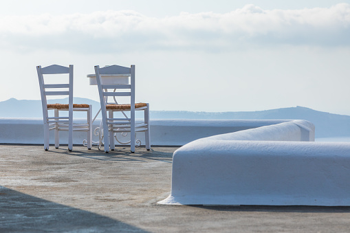 White chairs and tables on the terrace overlooking the caldera, Fira, Santorini Island, Greece.