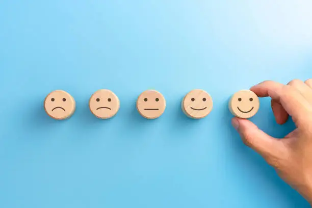 Photo of Customer service evaluation and satisfaction survey concepts. The client's hand picked the happy face smile face icon on wooden cube on blue background. copy space