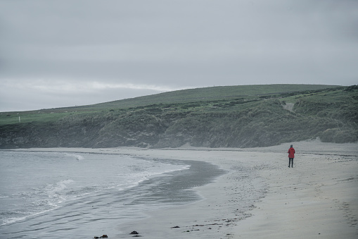 A woman is walking on a beach with fog on St Ninian Island in the Shetland Islands, Scotland.