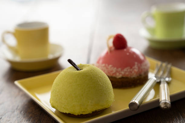 Two Small French ball shaped cakes mousse dome served on a plate with cups of tea