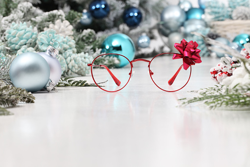 christmas eyeglasses red spectacles with ribbon bow isolated on white table with balls and decorations useful as a greeting gift card template with copy space