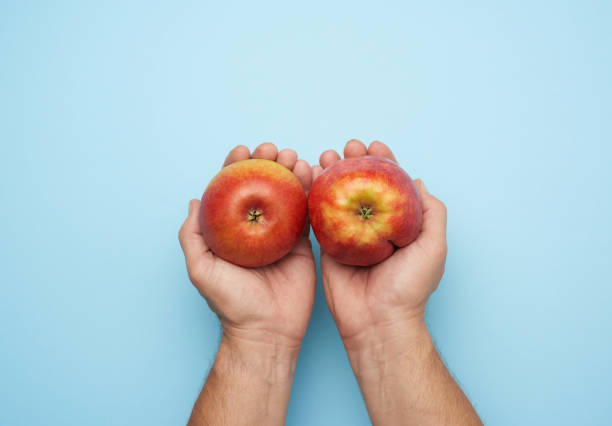 istock two male hands hold a ripe red apple on a blue background 1282493387