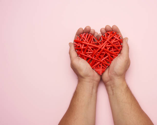 istock two male hands holding a red wicker heart on a pink background, 1282493691