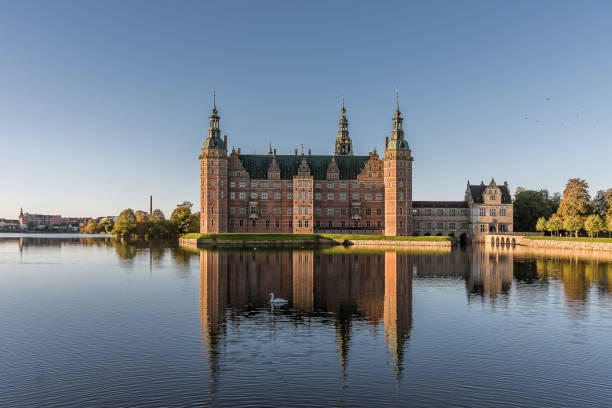 Frederiksborg Castle reflects in the lake a windless morning in the sunshine and a swa swims in the water,  Hillerød, Denm stock photo