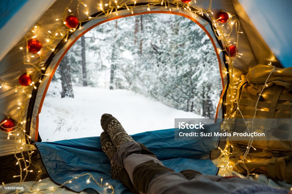 A man lying in a tent decorated with Christmas lights A man lying in a tent decorated with Christmas lights wearing warm wooden. Beautiful winter wild forest covered with snow. Self-isolation and social distancing during holidays. Christmas Stock Photo