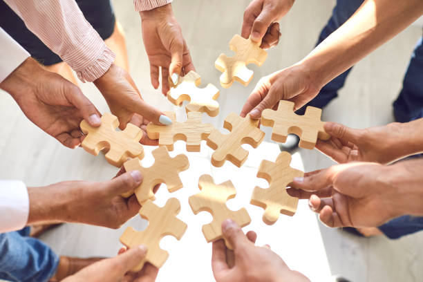 Company employees playing game and joining pieces of jigsaw puzzle during team building activity stock photo