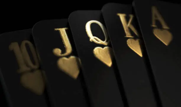 A fanned out royal flush suit of five black casino playing cards with gold markings on a dark classy background - 3D render