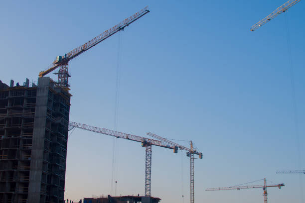 istock Silhouettes of tower cranes constructing a new residential building at a construction site against sunset background 1282504795