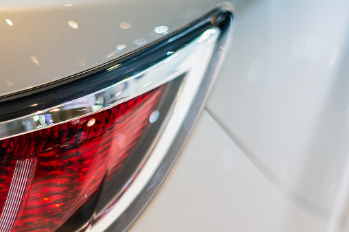 Close up detail of a red tail light with chrome surround on a white car with shallow focus and blurred background