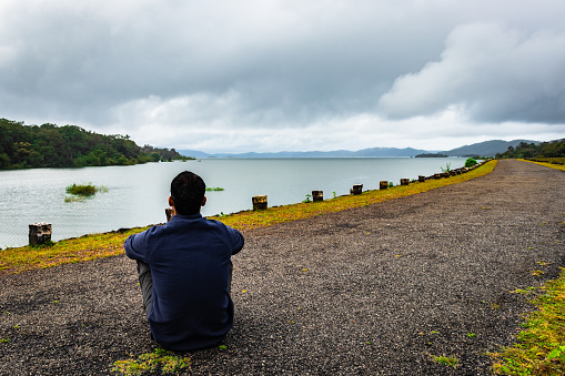 man young isolated watching the pristine nature at river edge with dramatic sky image is taken at supa dam dandeli karnataka india. it is showing the breathtaking beauty of nature at south india.