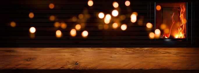 Illuminated rustic wooden table in front of an log fire with golden bokeh lights. Background for cozy evenings and space for your text and decorations.