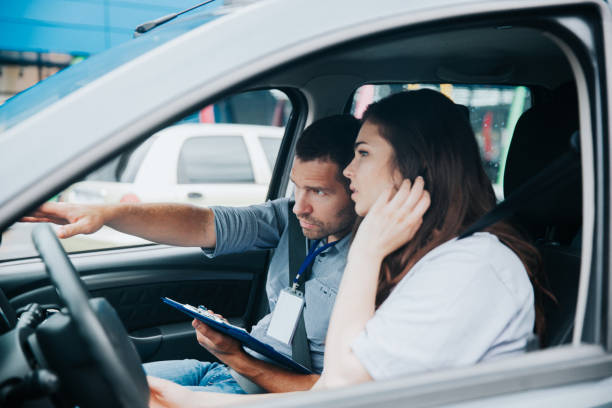 istock Male auto instructor explains driving rules to female student. Caucasian man points to the road and holds his paper. Young woman fixes her hair and listens to comments about her mistakes. 1282510742