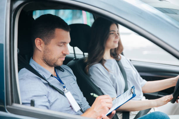 istock Learning to drive a car. Male instructor and female student practicing in driving. Young man notice results of test in his paper. Cheerful woman satisfied with driving lessons. 1282510837