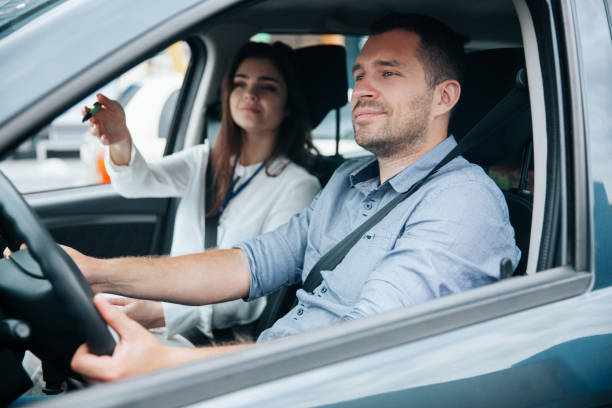 istock Female driving instructor pointing at object on road by her hand. Diligent male student driving the car and listening what his instructor is saying. Two people in car. Driving lessons concept. 1282510879