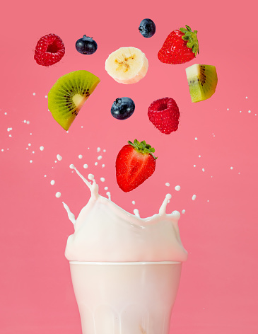 fruit mix falling into a splashing milk glass on color background