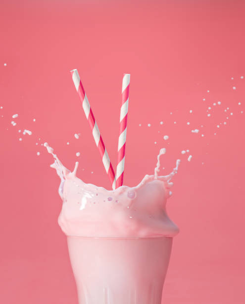 splashing berry milkshake on pink backdrop striped straws in a glass of splashing strawberry milkshake isolated on pastel pink color backdrop milkshake stock pictures, royalty-free photos & images