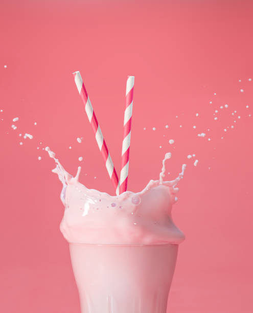 splashing berry milkshake on pink backdrop striped straws in a glass of splashing strawberry milkshake isolated on pastel pink color backdrop milkshake splash stock pictures, royalty-free photos & images