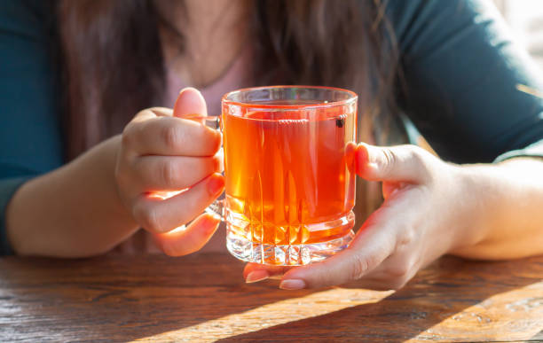 female hand holding hot cup of fruit tea on sunny morning - hot drink imagens e fotografias de stock