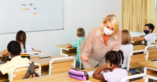 istock Teacher woman in protective mask helping schoolkid during lesson 1282518274