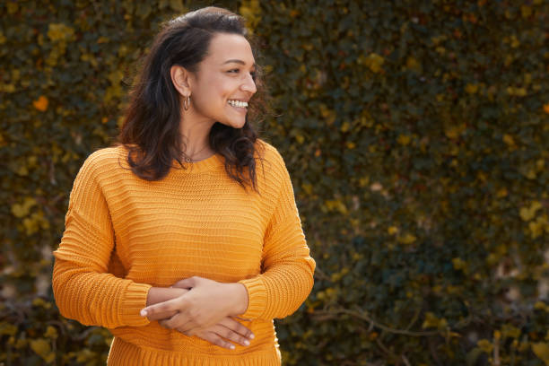 Portrait of beautiful happy woman in a yellow jumper Portrait of beautiful happy woman standing infront of leafy wall with hands on stomach on a lovely autumn day digestive system photos stock pictures, royalty-free photos & images