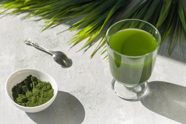 bebida saludable de cloro desintoxicación en vidrio y polvo sobre fondo ligero. superalimento, antioxidante natural para una dieta verde. efecto antienvejecimiento. sombras duras. - green drink fotografías e imágenes de stock