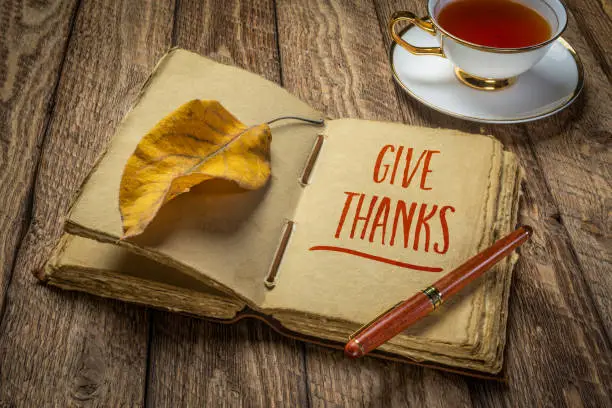 give thanks handwriting in antique leather-bound journal with decked edge handmade paper pages and a stylish pen on a rustic wooden table with a cup of tea, Thanksgiving and journaling concept