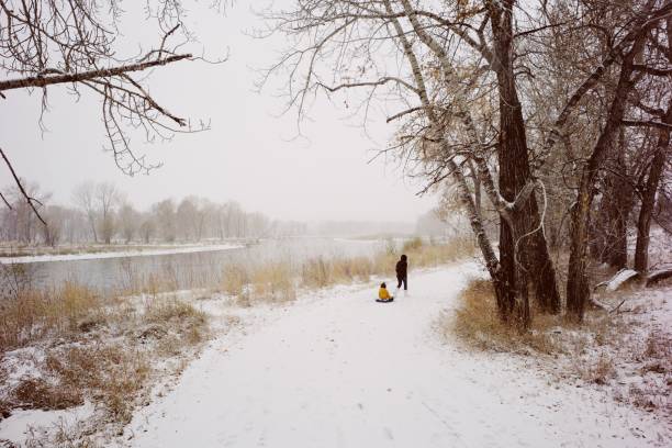 Mother pulling child in sled along the Bow River in Calgary, Canada