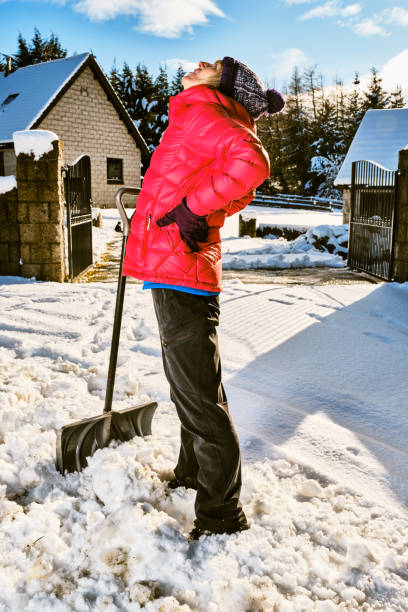 Senior woman has backache from clearing snow from her front yard with a snow shovel.