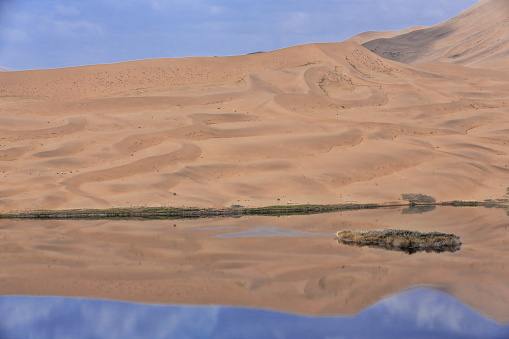 Lake Zhalate among the sand dunes of the Badain Jaran Desert-some reaching up to 500 meters-nomadic yurts on SE shore-clouds in the sky-megadune and sky reflection. Alxa Plateau-Inner Mongolia-China.