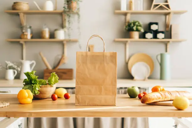 Photo of Eco shopping paper bag with fresh vegetables and baguette on table in kitchen