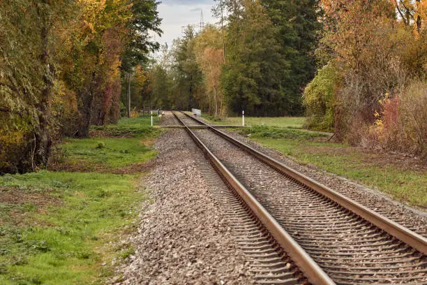 Railway track in autumn landscape surrounded by a forest. Diminishing perspective view of rails in rural area. Rastatt, Germany