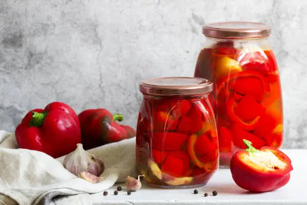 Pickled sweet peppers in glass jars on a light surface. Selective focus.