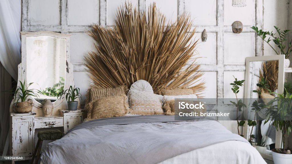 Cozy and comfortable room with interior in bohemian style Front view of cozy bedroom with interior design in boho chic style, comfortable bed, pillows, plaid and green houseplant decor near mirror on commode Bed - Furniture Stock Photo