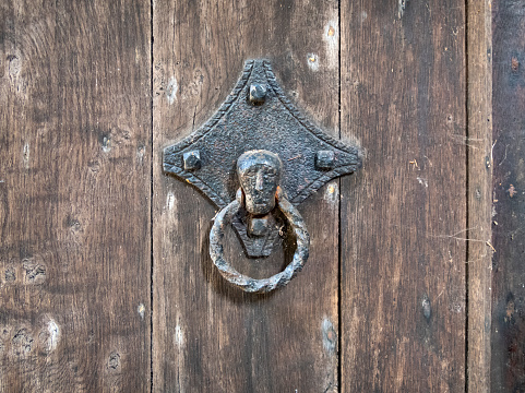 On the wooden door of an English church, an old metal knocker or handle with a sombre face.