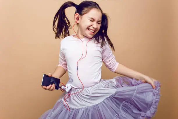 Closeup portrait of a amuse, little girl listening musin on her headphones, with closed eyes, posing in studio, on beige background.