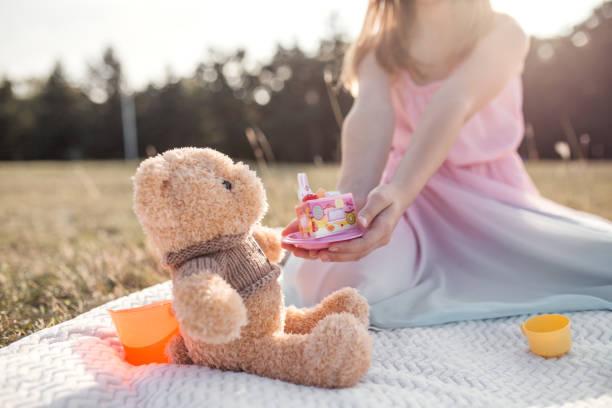 istock Young girl feeding her teddy bear with cake in park 1282546877