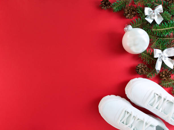 istock Holiday postcard with fir tree branches, cones, bows, bauble and trainers on a red background. Christmas flat lay with copy space. 1282546910