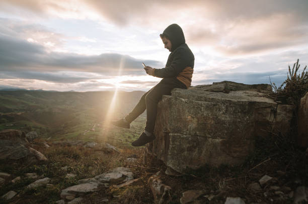 istock Young man sitting on top of a mountain using a smart phone 1282547056