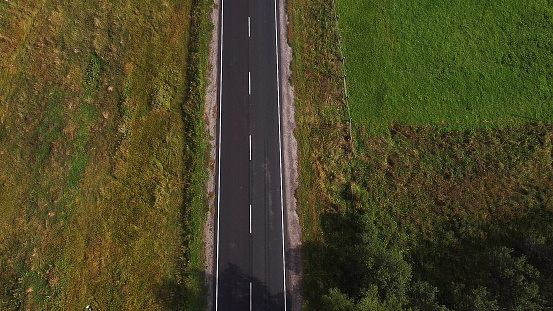 Aerial drone view of wide open empty road deep amongst wilderness forest with rolling hills and mountains.