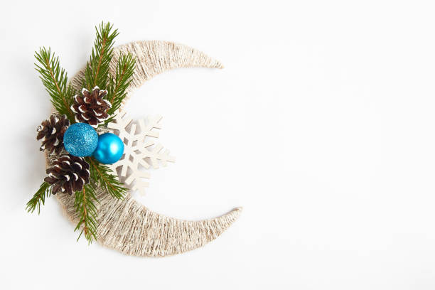 Photo of Fir tree branch, blue balls and pine cones on white crescent and snowflake. Top view with copy space. Flat lay. Christmas background or postcard. New year concept