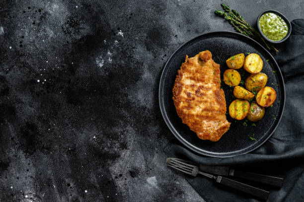 Breaded german weiner schnitzel with potatoes. Black background. Top view. Copy space Breaded german weiner schnitzel with potatoes. Black background. Top view. Copy space. fried potato stock pictures, royalty-free photos & images